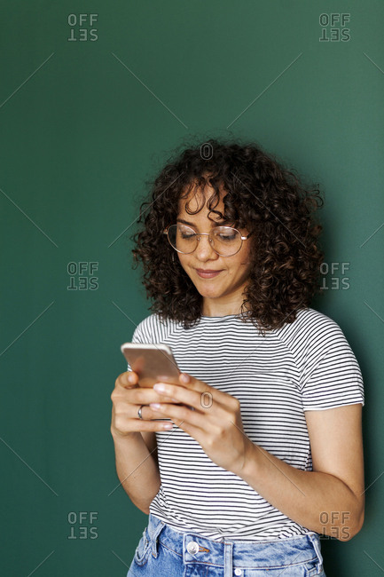 Woman using smart phone while standing against green wall