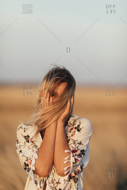 Portrait of a young woman with windblown hair and hands on face