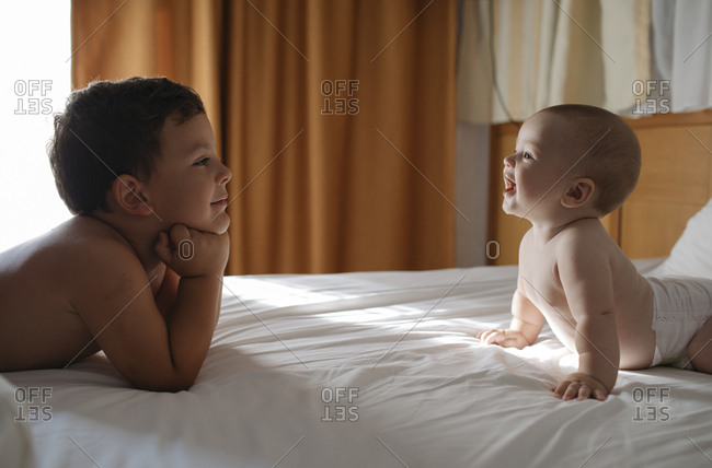Older brother and baby brother on bed looking at each other