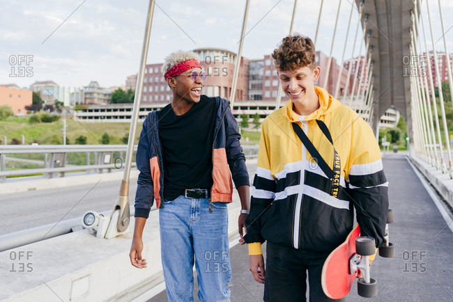 Two handsome teenage boys with skateboard walking and laughing on the bridge