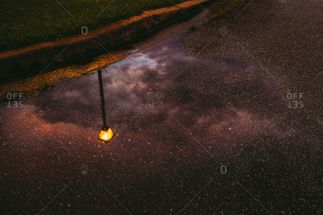 Reflection of streetlamp and cloudy sky in puddle on the side of the road