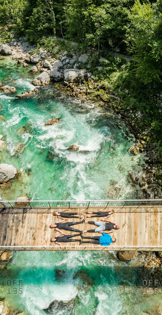 Aerial view of sporty family lying on wooden suspension bridge above a river.