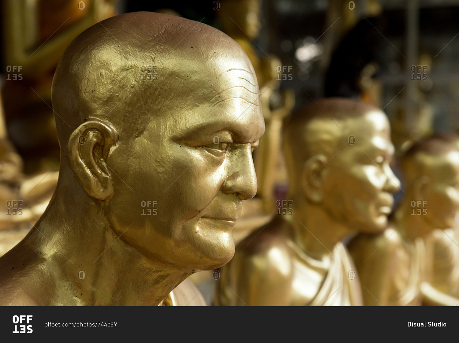 Side view of row of golden shiny statues of monks stock photo OFFSET