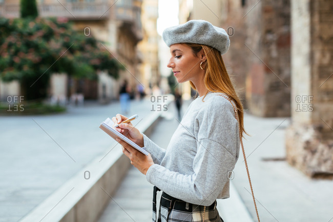 Chic woman wearing beret writing on notebook on the street.