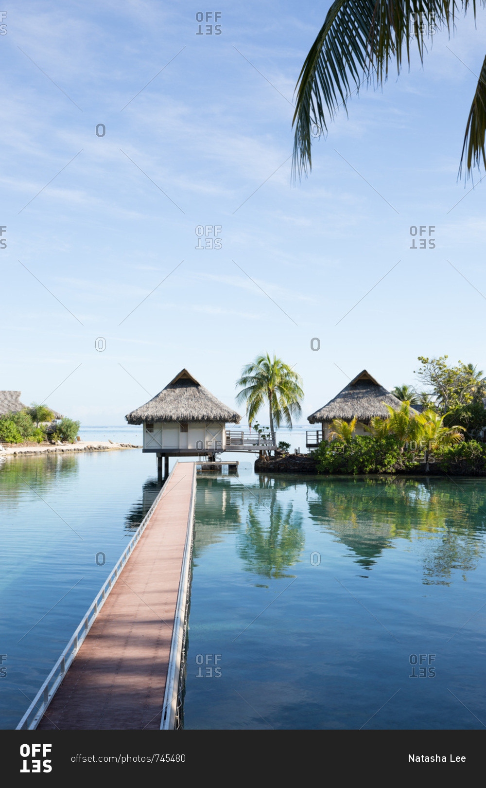 Overwater bungalows at end of long walkway over blue waters of lagoon on tropical island