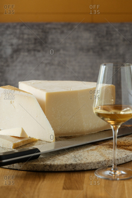 Cheese on a marble cutting board with a knife and a glass of white wine