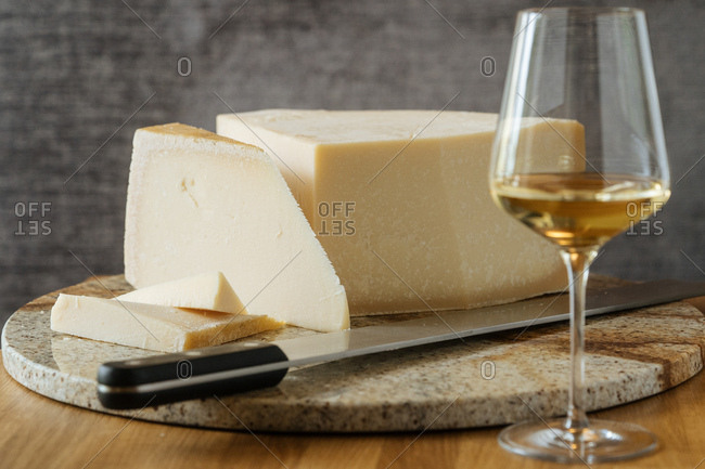 Cheese on a marble cutting board with knife and glass of white wine