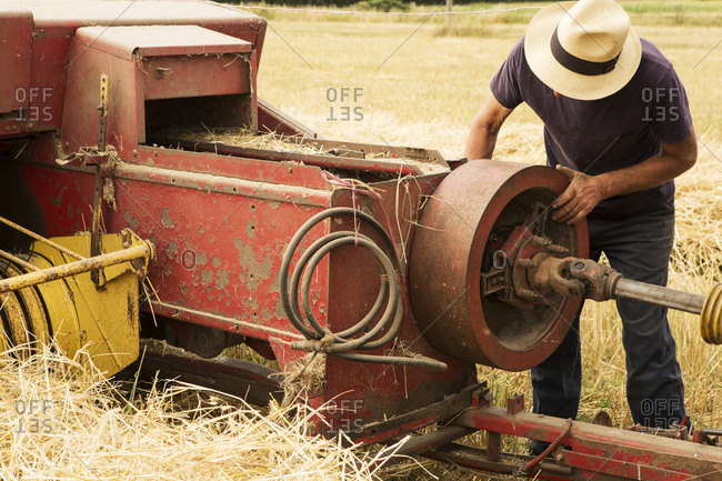 Tractor and straw baler in wheat field, farmer checking equipment.