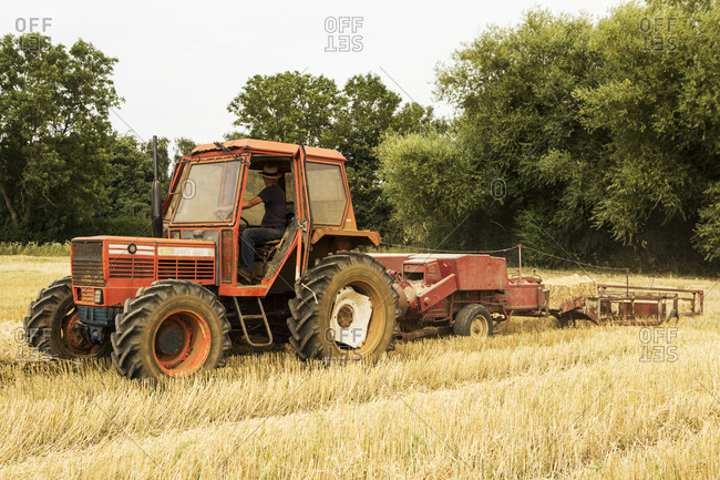 Tractor and straw baler in wheat field, farmer baling straw.