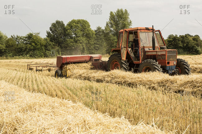 Tractor and straw baler in wheat field, farmer baling straw.