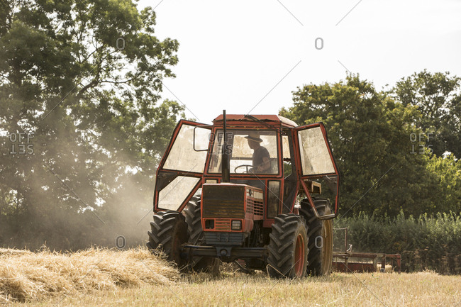 Tractor and straw baler in wheat field, farmer baling straw.