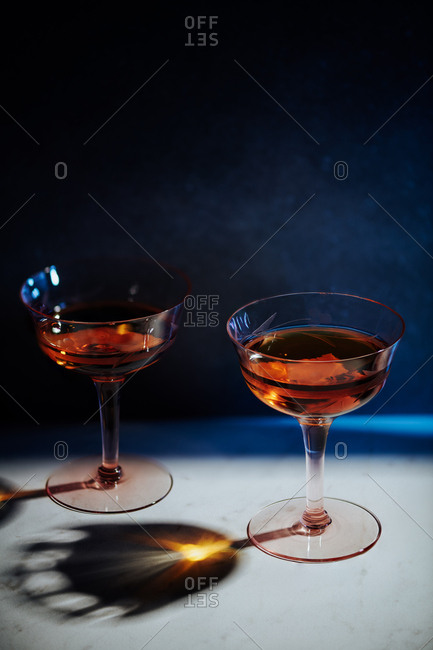 Classic Manhattan of whiskey, sweet vermouth and bitters served in two vintage depression era glasses served in a simple setting in hard light.