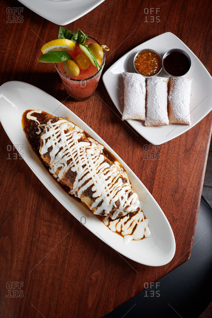 Breakfast chimichanga covered in a mole sauce served with beignets and a bloody mary for brunch or breakfast.