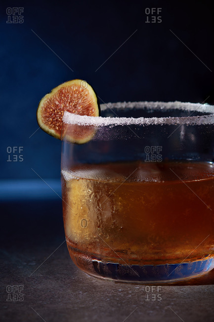 Cinnamon Fig Sidecar consisting of sour, cinnamon, orange curacao cognac, served in a rocks tumbler glass with a sugar rim and garnished with a black fig.