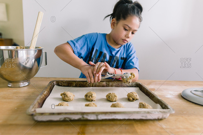 Girl scooping cookie dough onto sheet pan in kitchen