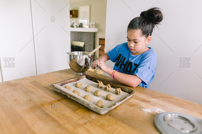 Girl scooping chocolate chip cookie dough onto sheet pan