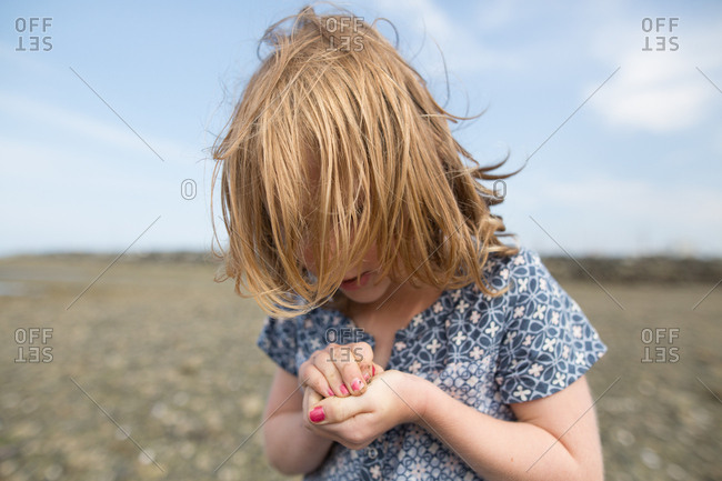 Girl on rocky beach looking down at cupped hands