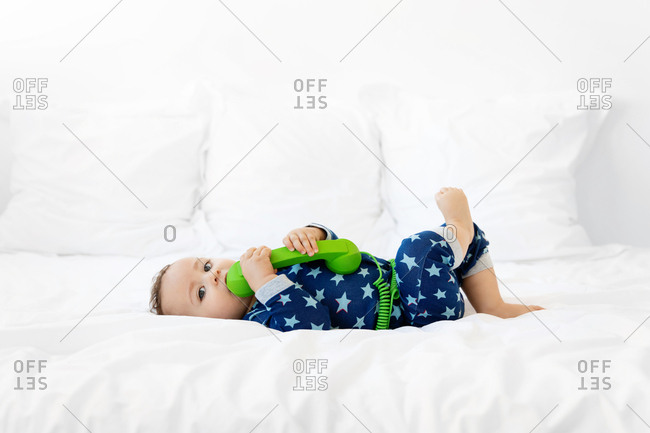 Baby lying on white bed chewing on green phone
