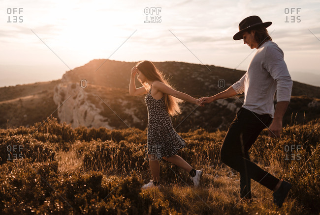 Side view of young vintage couple walks by a cliff in a sunset of summer mountains background