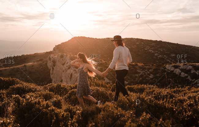 Side view of young vintage couple walks by a cliff in a sunset of summer mountains background