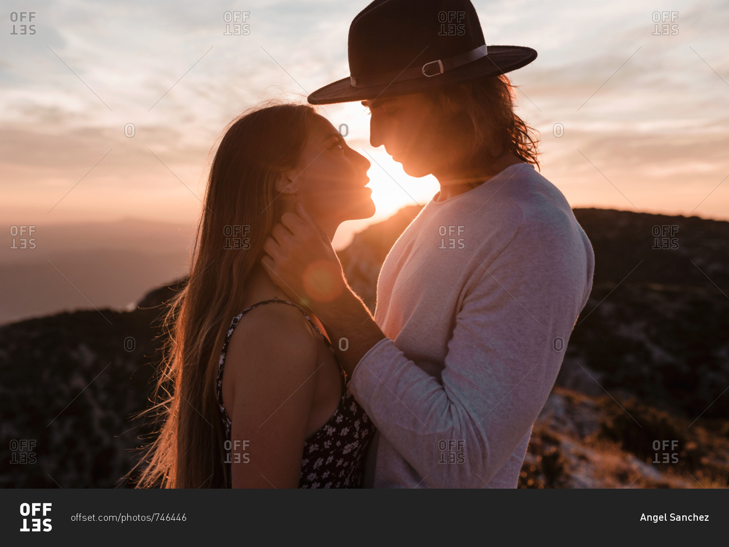 Side view of young vintage couple hugs and kissing in a cliff in a sunset mountains background