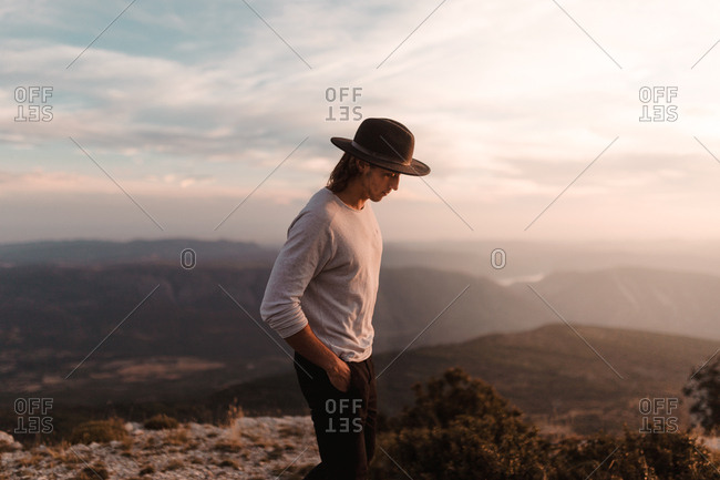 Portrait of young vintage blond man with black hat and long hair looking at camera in a cliff mountains background