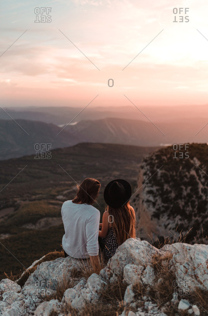 Rear view of vintage couple in a cliff observing the horizon in a sunset of summer mountains background