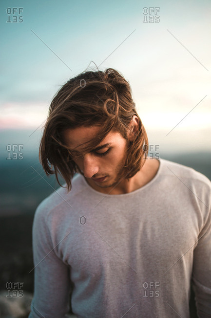 Portrait of young vintage blond man with long hair looking at camera in a cliff mountains background