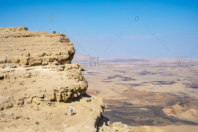 Distant view shot of hiker standing near edge of Makhtesh Ramon Crater, Negev Desert, Mitzpe Ramon, Southern District, Israel