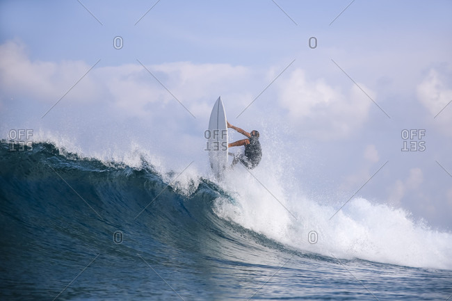 Male surfer riding wave against clouds, Male, Maldives