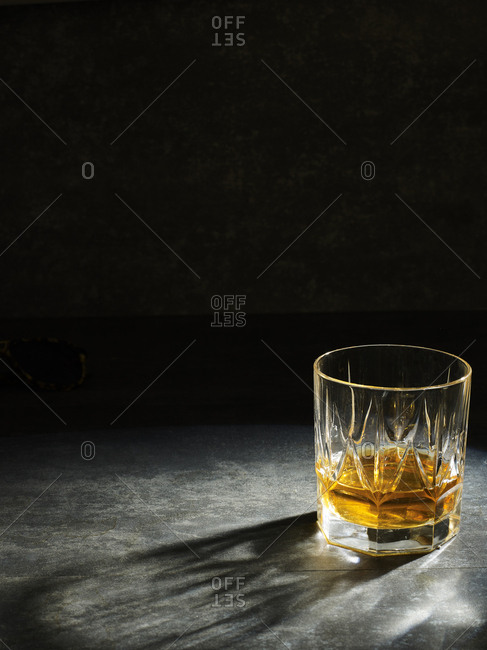 Close-up of clear crystal glass filled with golden liquor on gray background in shadow of grid