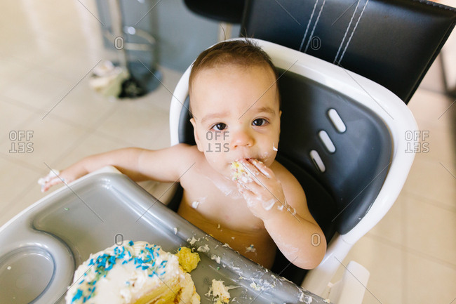 Baby sitting in high chair eating birthday cake