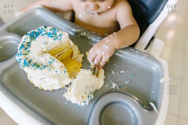 Baby sitting in high chair with hand in frosting of birthday cake