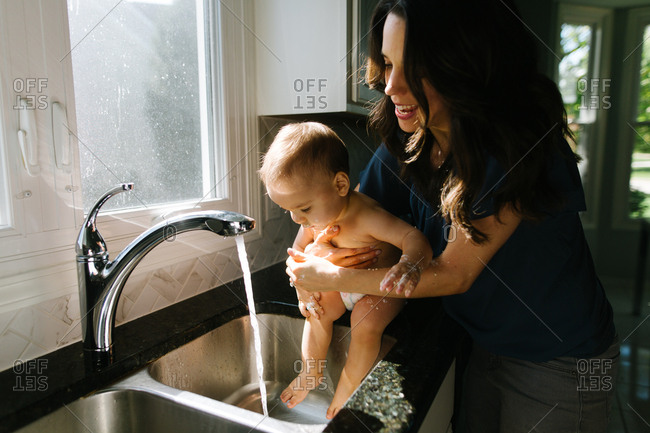 Mother washing off baby in kitchen sink