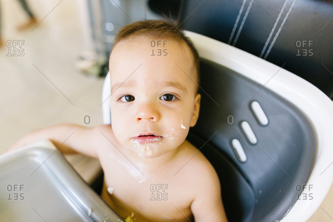 Portrait of a baby with messy face from cake frosting sitting in high chair