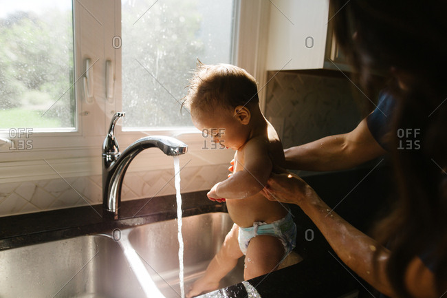 Mother bathing baby in kitchen sink