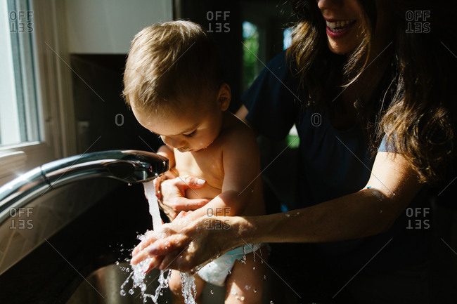 Mother splashing water while bathing baby in kitchen sink