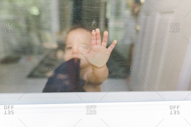 Baby pressing hand against window screen