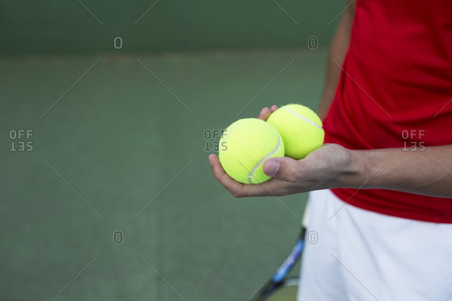Unrecognizable sportsman holding two balls while standing on tennis court
