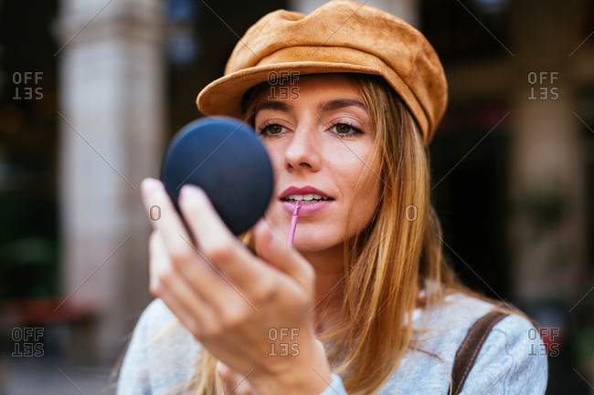 Chic woman wearing beret checking makeup on the street.