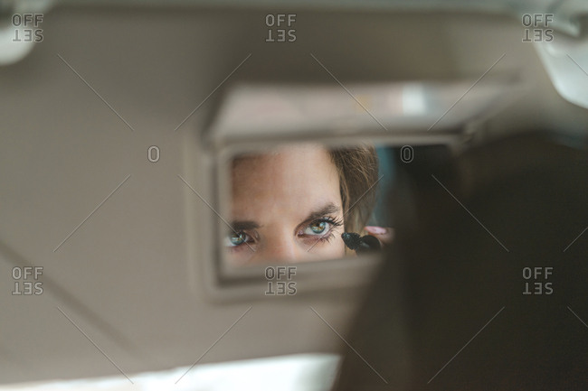 Woman mirrored in rear view mirror applying mascara in car
