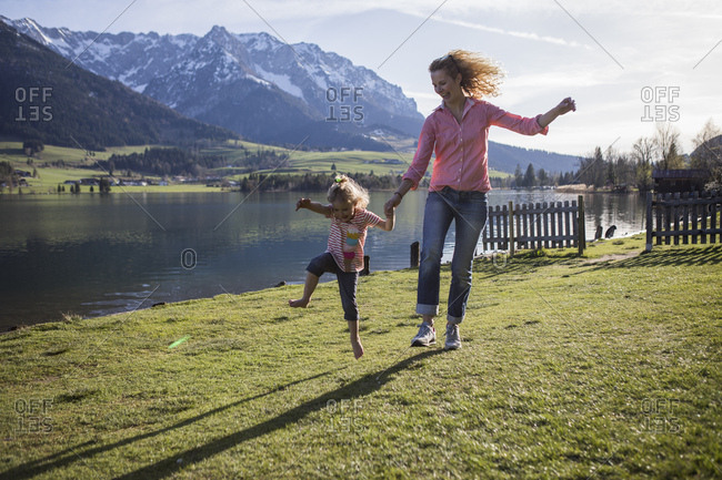 Austria- Tyrol- Walchsee- carefree mother and daughter jumping at the lake