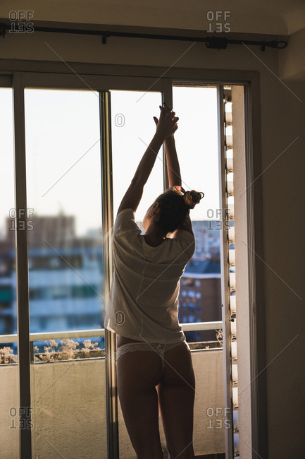 Young woman in t-shirt and panties at home standing at the window stock  photo - OFFSET