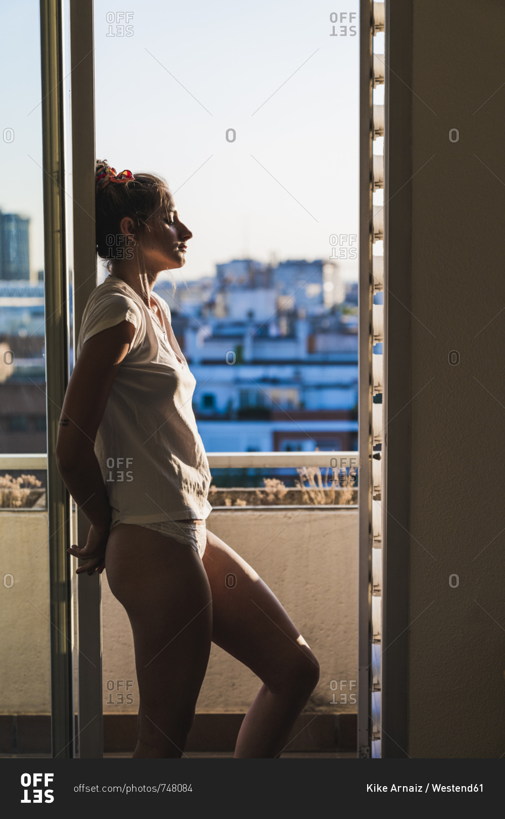 Young woman in t-shirt and panties at home standing at the window stock  photo - OFFSET