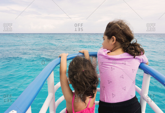 Two sisters watching the ocean from the railing of a boat