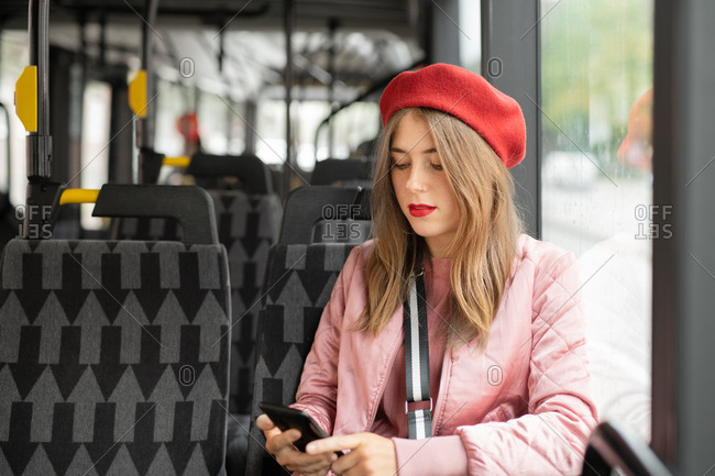 Young woman wearing red beret using cell phone while riding bus