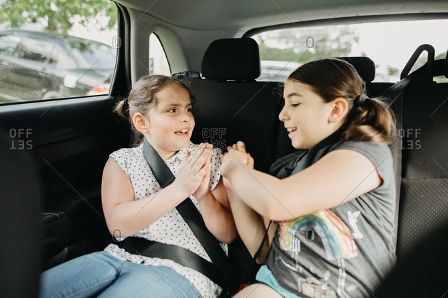 Two girls playing hand clapping games in the backseat of a car