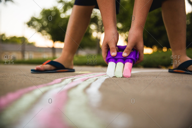 Child drawing on sidewalk with three pieces of chalk