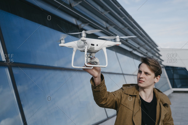 Young man holding a drone with a large glass building in the background