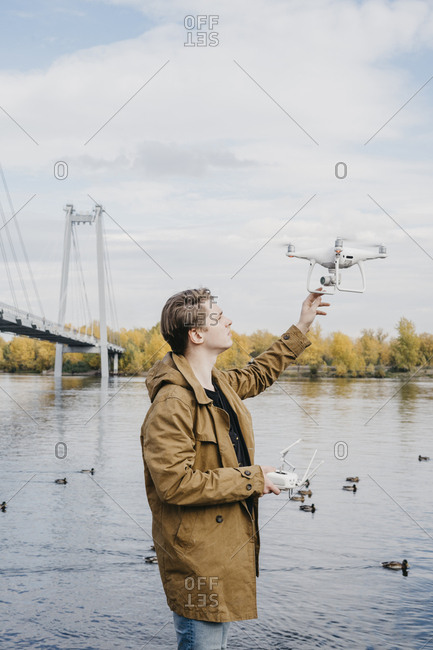 Young man flying his drone along a riverfront with a large bridge in the background